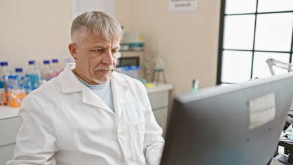 A mature grey-haired scientist in a lab coat working on a computer in a laboratory setting