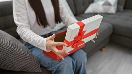 Asian woman opening red ribbon gift box in a modern living room