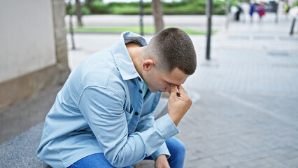 Obraz premium Thoughtful young hispanic man sitting outdoors on a city street, posing for a lifestyle portrait.