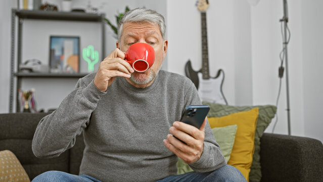 Mature man with smartphone and coffee in a modern living room.