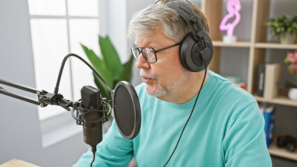 Mature man with headphones speaks into microphone in a podcast studio setting