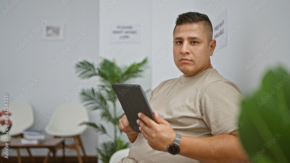 Sticker casual young latin man, plugged into his online world, sitting relaxed in a waiting room chair, inte