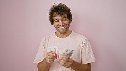 Handsome young man smiling while holding icelandic kronur against a pink background