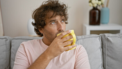 Handsome young hispanic man drinking coffee in a modern living room interior.