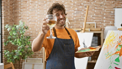 A happy hispanic man toasting in an art studio with a glass of wine.