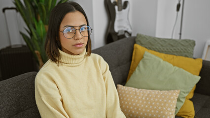 Hispanic woman with glasses wearing yellow sweater sitting on couch indoors