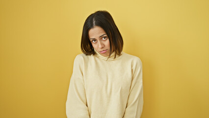 Fototapeta premium Portrait of a young hispanic woman with a neutral expression, wearing a sweater against a yellow background.