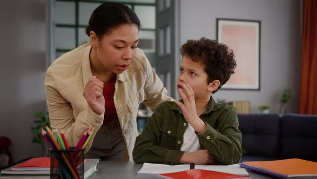 African American family little boy child kid son pupil studying home education homework learning study problem tired boring sad angry mother woman female mom come in room talking dissatisfied scold