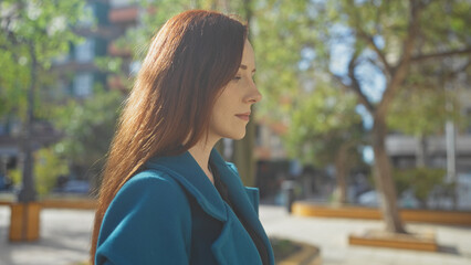 A contemplative young woman in a stylish teal coat enjoys a peaceful urban park setting with...