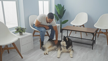 A young hispanic man petting a husky dog indoors at a modern veterinary clinic.