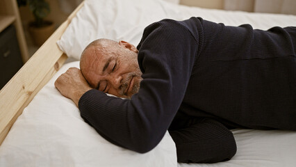 A middle-aged bearded man with grey hair sleeping peacefully in a bedroom setting, conveying a...