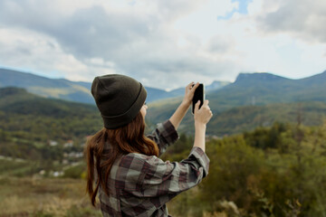 Adventurous woman capturing breathtaking mountain scenery on cell phone during travel excursion