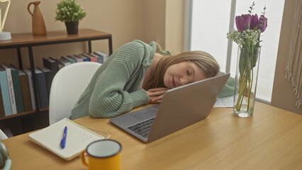 A woman rests her head on a laptop in a cozy room, suggesting tiredness or relaxation amidst casual...