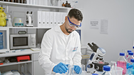 A young man with a beard works meticulously in a lab, surrounded by scientific equipment and...