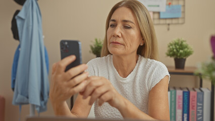A middle-aged caucasian woman uses a smartphone in a well-lit living room, expressing contemplation...