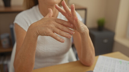 A middle-aged woman with joint pain in her hands indoors at her home, possibly dealing with arthritis symptoms.