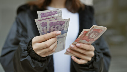A young hispanic woman counts colombian currency on a city street.