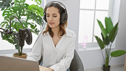 Hispanic woman records podcast indoors with professional microphone and headphones.