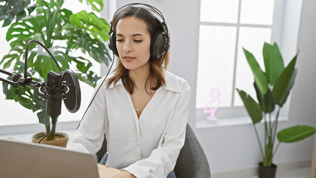 Hispanic woman records podcast indoors with professional microphone and headphones.