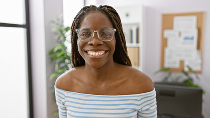 Smiling african american woman with braids wearing glasses in a bright office interior.