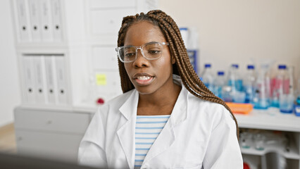 African american woman with braids wearing lab coat and glasses in a laboratory setting.
