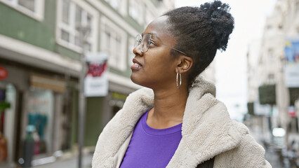 Confident african-american woman in stylish urban attire stands thoughtfully on a busy city street.
