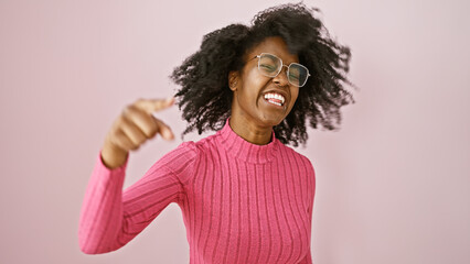 Portrait of a joyful african woman dancing indoors wearing glasses and pink attire.