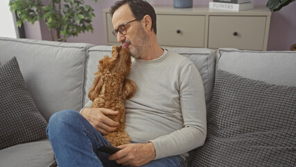 Hispanic senior man affectionately interacts with his poodle in a cozy living room.