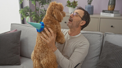 A middle-aged man joyfully interacts with his playful poodle in a cozy, modern living room.