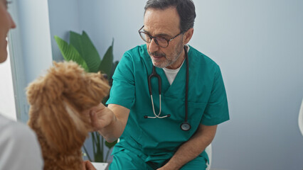 A middle-aged hispanic veterinarian man examines a poodle dog indoors at a vet clinic.