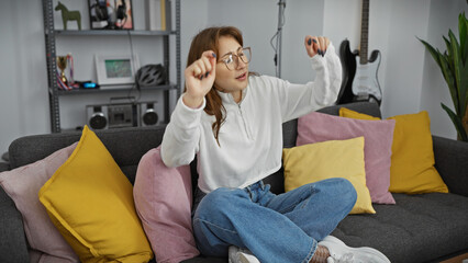Obraz premium A young caucasian woman dances joyfully in a cozy living room setting, embodying leisure and relaxation at home.