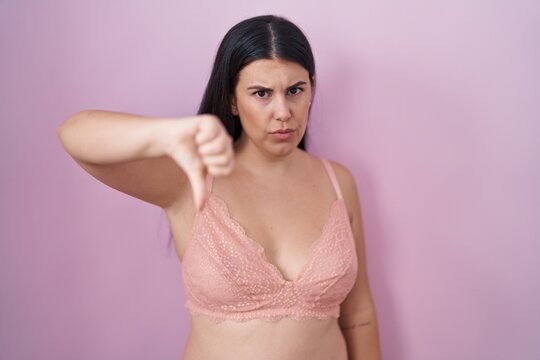 Young hispanic woman wearing pink bra looking unhappy and angry showing rejection and negative with thumbs down gesture. bad expression.