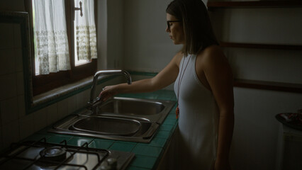 Young hispanic woman in a typical old italian house, standing by the sink in a dimly lit kitchen with vintage decor. - Powered by Adobe