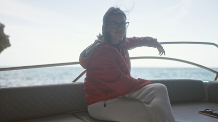 A young hispanic woman wearing a red jacket enjoys a serene boat ride on the sea in a picturesque...