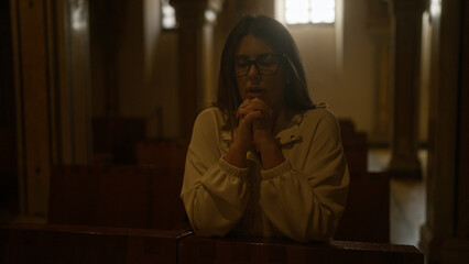 A young hispanic woman prays in an italian christian church, showcasing religious devotion and...