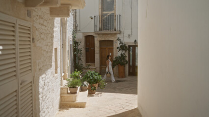 A young hispanic woman strolling through the charming, sunlit streets of locorotondo in puglia,...