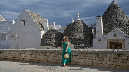 Beautiful young hispanic woman in a green dress stands on a cobblestone street in the old town of...