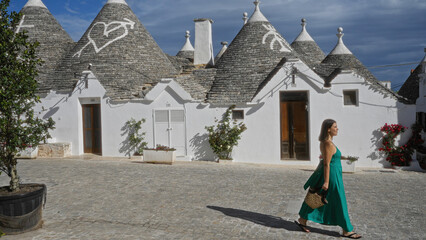 Young hispanic woman in a green dress walking past traditional trulli houses in the old town of...