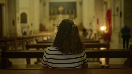 A young hispanic woman sits alone in a beautiful historic christian church in italy, gazing towards...