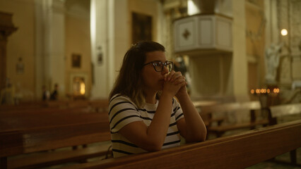 A young hispanic woman is seen praying inside a beautiful italian church, providing a serene religious ambiance.