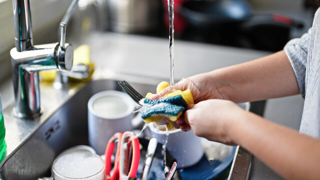Young beautiful hispanic woman washing plates at the kitchen