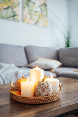 Autumn fall cozy mood composition for hygge home decor. Orange pumpkins decorated with mandalas, burning candles on wicker tray on the coffee table in the living room. Selective focus. Copy space.