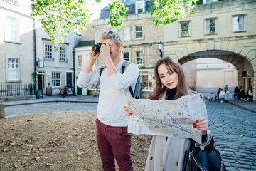 Fun, friends, travel and tourism concept. Young woman looking for direction on map during travel walk in old European city. Tourists using city guide map and camera. Explore a new city together