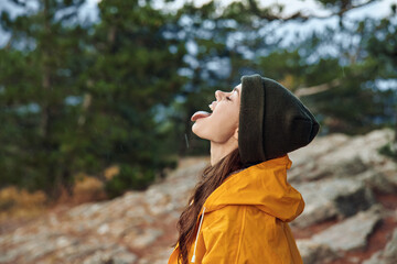 A young woman in a yellow raincoat standing on a rocky hill with mouth open in awe of natural...