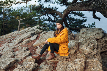 Woman in a yellow coat enjoying a peaceful moment in nature, surrounded by pine trees