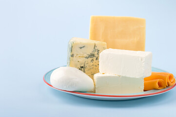 Several types of cheese on a plate on a blue background, horizontal. Composition of mozzarella, buko, dor blue, gouda, cheddar. Assorted dairy products.