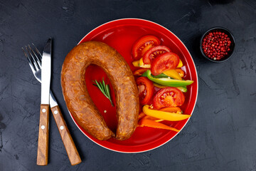 Red plate and pieces of salami sausage with vegetables and spices , top view