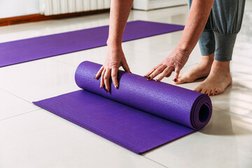 Senior woman rolling up her exercise mat after a yoga class.