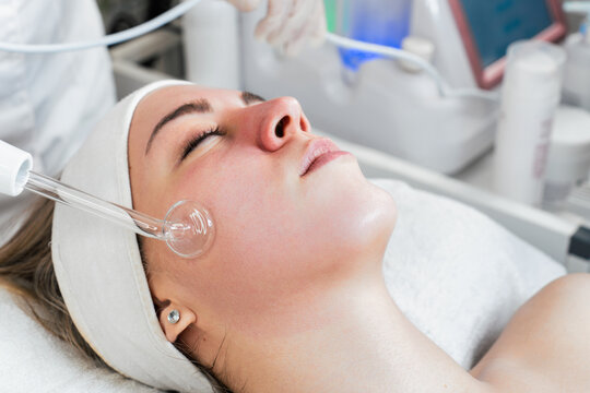 Young woman receiving face lift treatment with high-frequency wand. This modern treatment uses electric currents to kill acne-causing bacteria, reduce inflammation, and improve skin tone and texture.