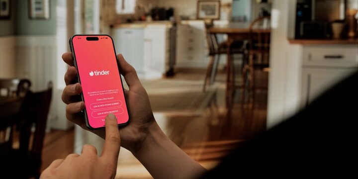 Hand holding a smartphone with Tinder app open, ready to swipe in a cozy home setting